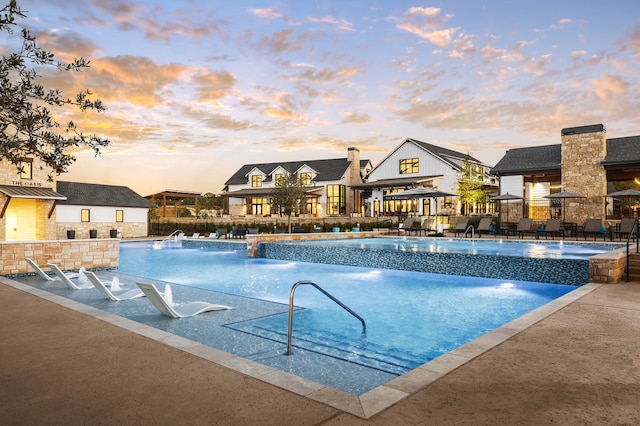 pool at dusk with a patio area and pool water feature