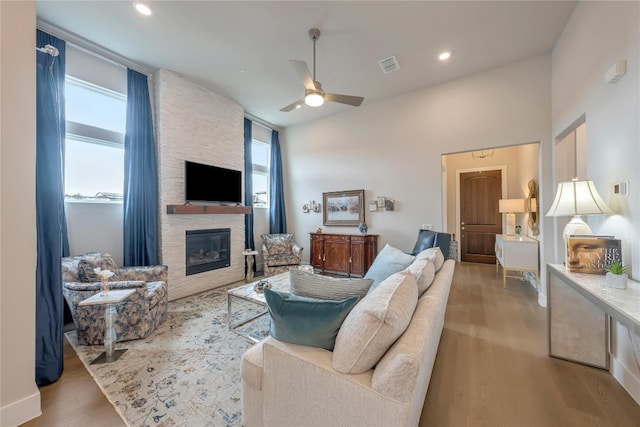 living room with a stone fireplace, light hardwood / wood-style floors, and ceiling fan