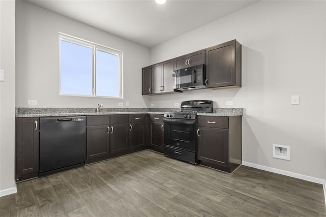 kitchen featuring dark brown cabinetry, light stone countertops, sink, dark hardwood / wood-style flooring, and black appliances