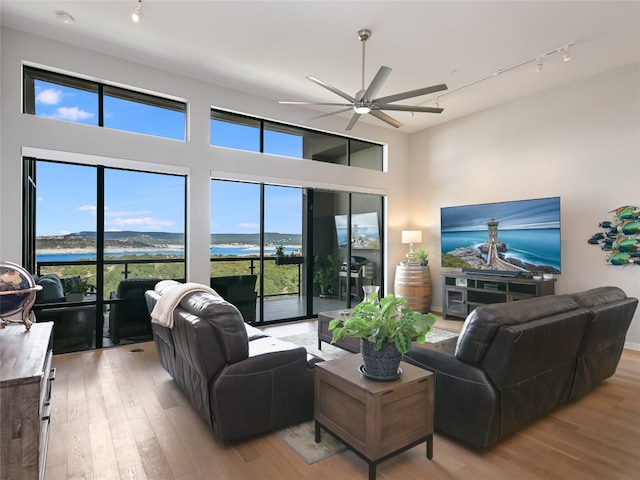 living room featuring ceiling fan, hardwood / wood-style floors, track lighting, and a water view