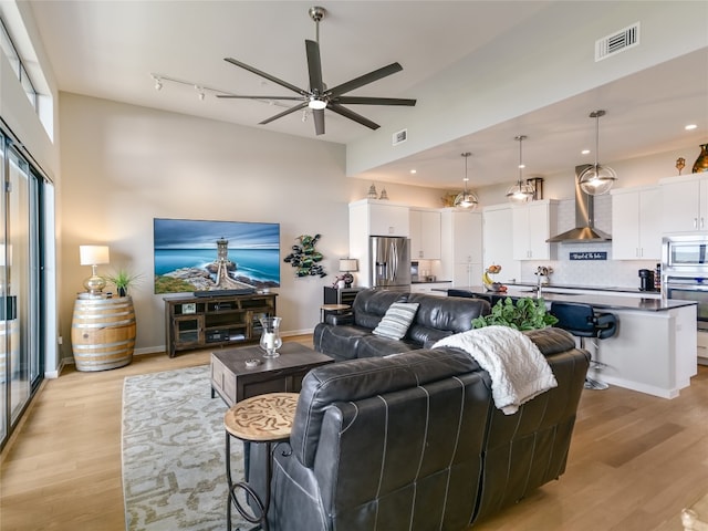 living room with light wood-type flooring, a high ceiling, sink, track lighting, and ceiling fan