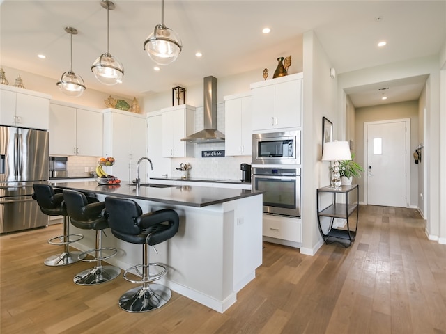 kitchen with wall chimney range hood, wood-type flooring, backsplash, and appliances with stainless steel finishes