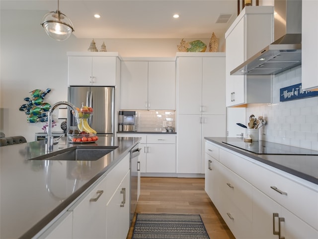 kitchen with hanging light fixtures, stainless steel appliances, light wood-type flooring, backsplash, and wall chimney range hood