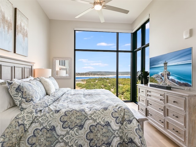 bedroom featuring light wood-type flooring, a water view, and ceiling fan