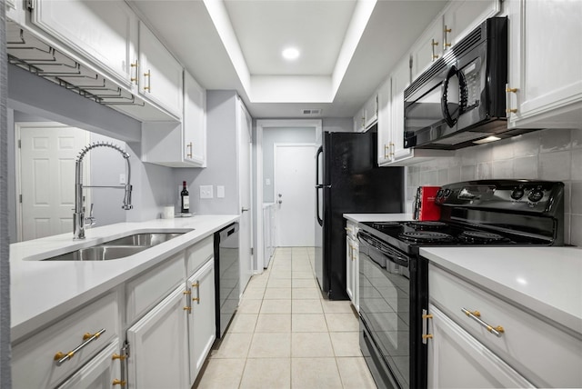 kitchen featuring a tray ceiling, black appliances, white cabinets, sink, and light tile floors