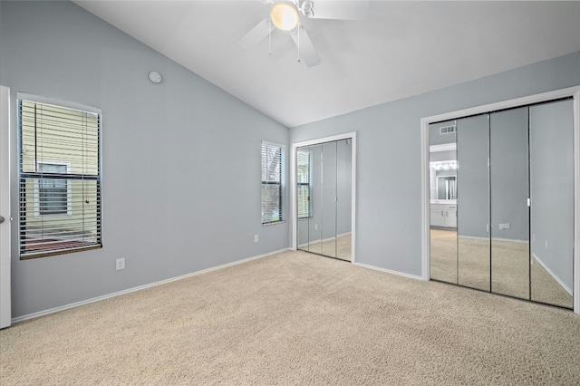 unfurnished bedroom with two closets, lofted ceiling, ceiling fan, and light colored carpet