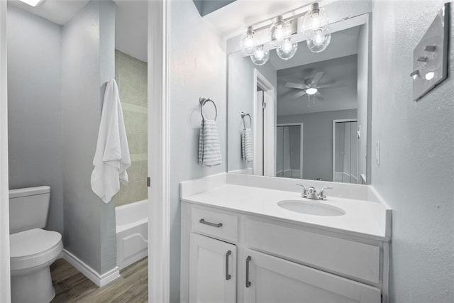 full bathroom featuring ceiling fan, vanity with extensive cabinet space, tiled shower / bath combo, wood-type flooring, and toilet