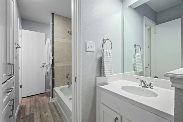 bathroom with tiled shower / bath combo, vanity, and wood-type flooring