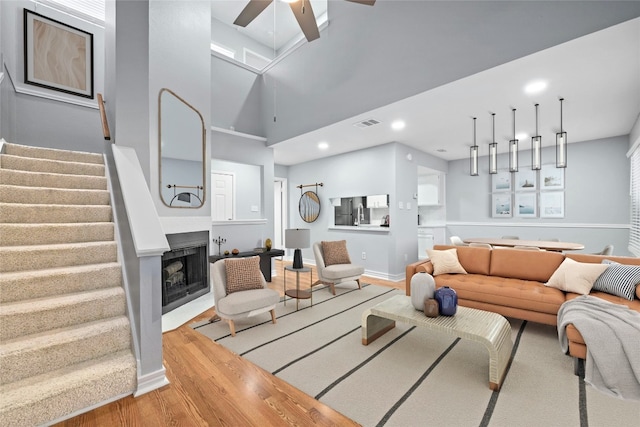 living room featuring a high ceiling, ceiling fan, and light wood-type flooring