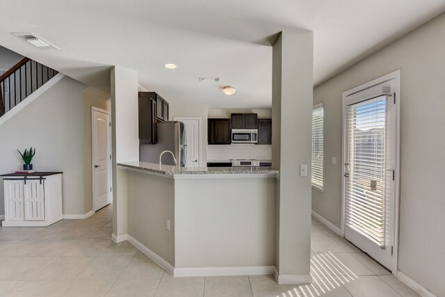 kitchen featuring backsplash, dark brown cabinetry, light stone countertops, appliances with stainless steel finishes, and light tile patterned floors