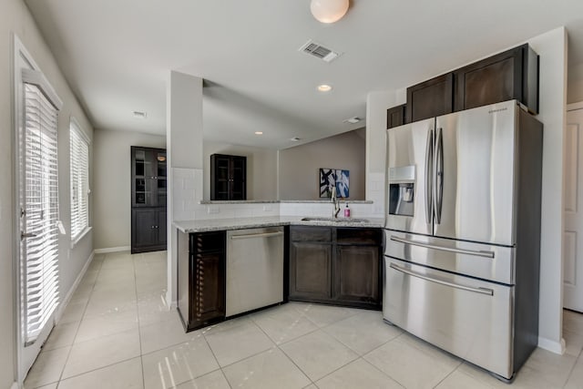 kitchen featuring stainless steel appliances, decorative backsplash, light tile patterned flooring, light stone counters, and dark brown cabinets