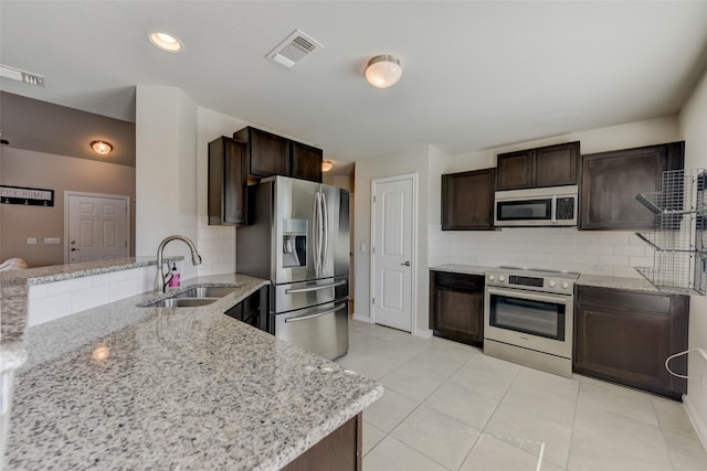 kitchen featuring dark brown cabinetry, stainless steel appliances, sink, backsplash, and light stone counters