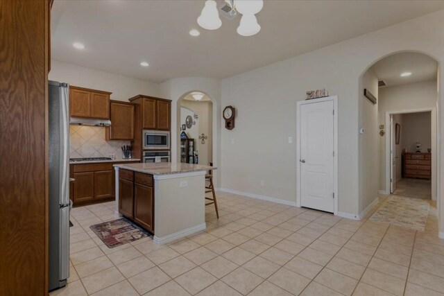 kitchen featuring backsplash, a breakfast bar, appliances with stainless steel finishes, light tile patterned floors, and a center island