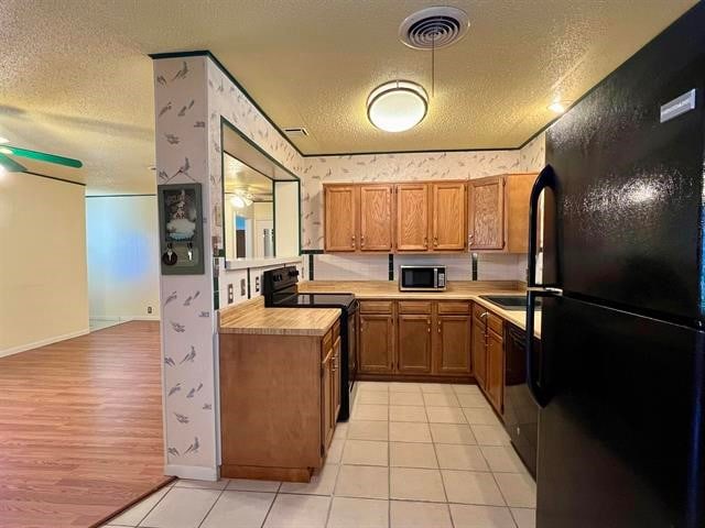 kitchen featuring a textured ceiling, light hardwood / wood-style floors, ceiling fan, and black appliances