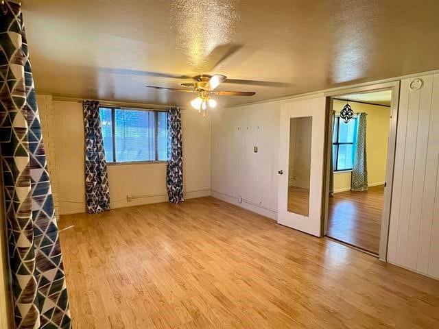 empty room with light hardwood / wood-style floors, ceiling fan, a textured ceiling, and a wealth of natural light