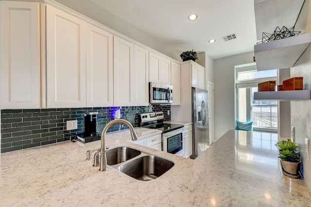 kitchen with appliances with stainless steel finishes, sink, white cabinets, and light stone countertops