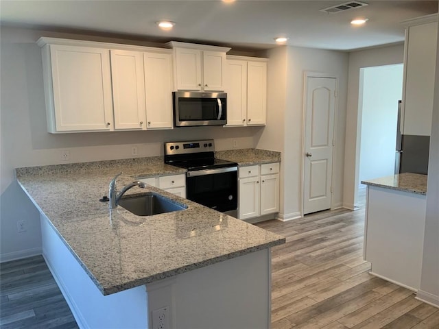 18624 Allen Welch Dr, Elgin, TX 78621 - kitchen featuring stainless steel appliances, light wood finished floors, white cabinetry, a peninsula, and recessed lighting