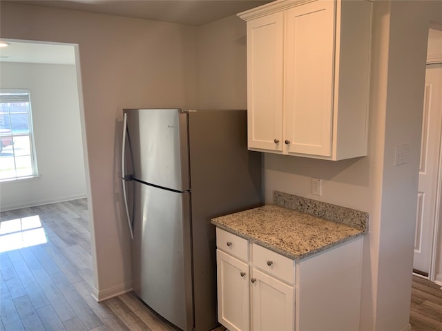 kitchen featuring stainless steel refrigerator, white cabinetry, light hardwood / wood-style flooring, and light stone counters