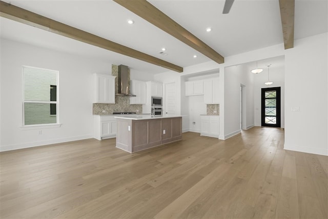 kitchen featuring white cabinets, stainless steel appliances, light hardwood / wood-style floors, wall chimney range hood, and a center island with sink