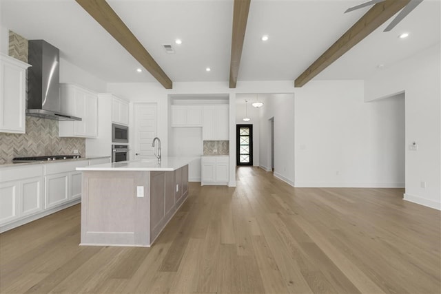 kitchen with a kitchen island with sink, white cabinetry, light hardwood / wood-style flooring, stainless steel appliances, and wall chimney exhaust hood