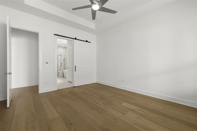 unfurnished bedroom with a barn door, ceiling fan, hardwood / wood-style flooring, and ensuite bathroom