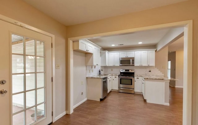 kitchen with appliances with stainless steel finishes, light wood-type flooring, backsplash, white cabinetry, and light stone countertops