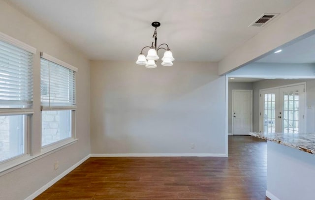 spare room with dark hardwood / wood-style floors, a healthy amount of sunlight, french doors, and an inviting chandelier