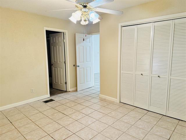 unfurnished bedroom with light tile patterned flooring, a closet, and ceiling fan