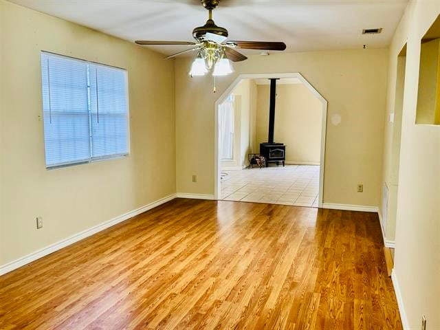 unfurnished living room featuring light wood-type flooring, a wood stove, and ceiling fan