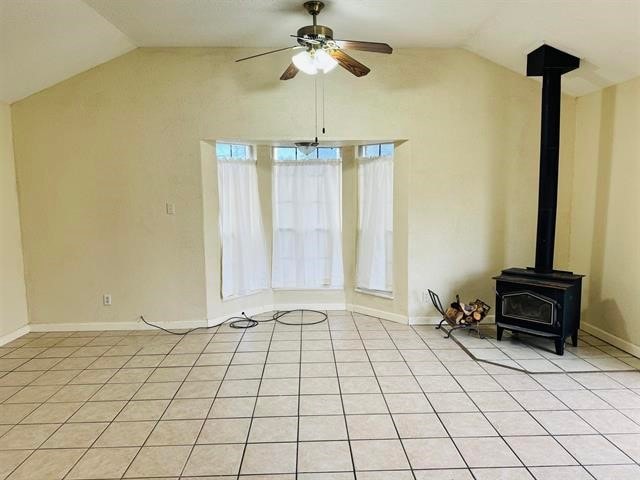 unfurnished living room featuring a wood stove, ceiling fan, plenty of natural light, and lofted ceiling