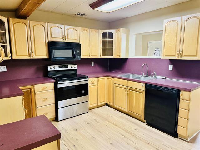 kitchen with sink, light hardwood / wood-style flooring, beamed ceiling, light brown cabinetry, and black appliances