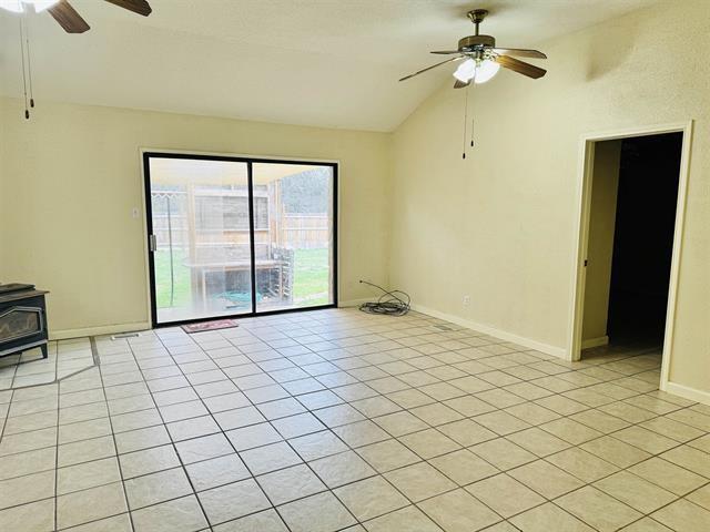 tiled empty room with a wood stove, ceiling fan, and vaulted ceiling