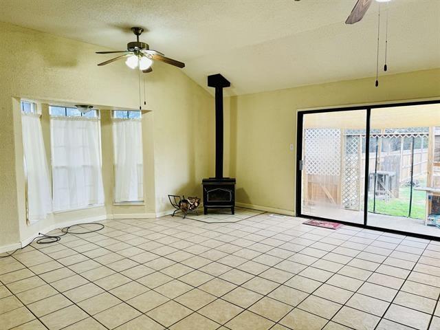 unfurnished living room featuring lofted ceiling, ceiling fan, a wood stove, and light tile patterned floors