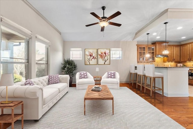 living room featuring wood-type flooring, vaulted ceiling, crown molding, and ceiling fan