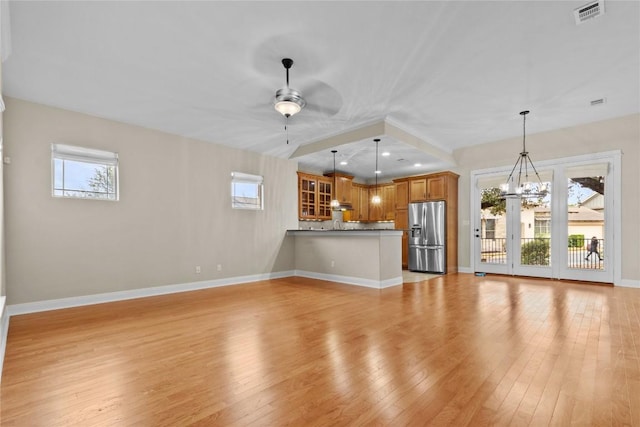 unfurnished living room with plenty of natural light, ceiling fan with notable chandelier, and light wood-type flooring