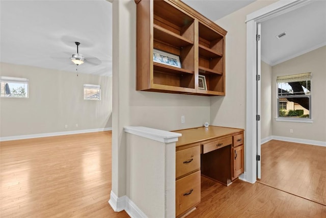 unfurnished office featuring ceiling fan, lofted ceiling, built in desk, and light wood-type flooring