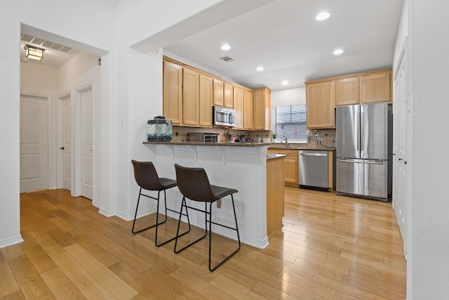 kitchen featuring kitchen peninsula, a kitchen breakfast bar, light hardwood / wood-style floors, stainless steel appliances, and tasteful backsplash