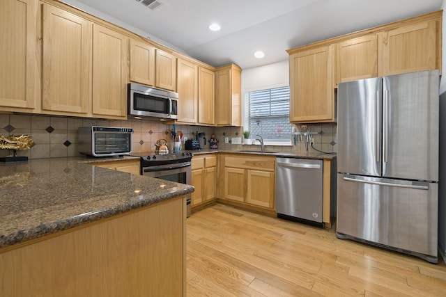 kitchen featuring appliances with stainless steel finishes, dark stone counters, light hardwood / wood-style floors, and tasteful backsplash