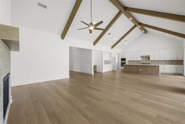 unfurnished living room featuring ceiling fan, beam ceiling, high vaulted ceiling, a fireplace, and light hardwood / wood-style flooring