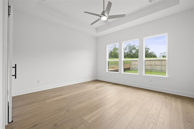 empty room featuring ceiling fan, a tray ceiling, and light hardwood / wood-style floors