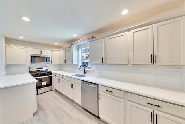 kitchen featuring light hardwood / wood-style floors, white cabinetry, stainless steel appliances, backsplash, and sink