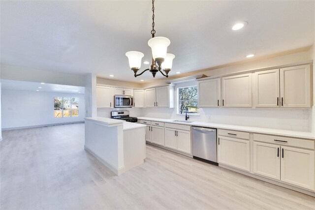 kitchen featuring stainless steel appliances, light wood-type flooring, pendant lighting, sink, and a chandelier