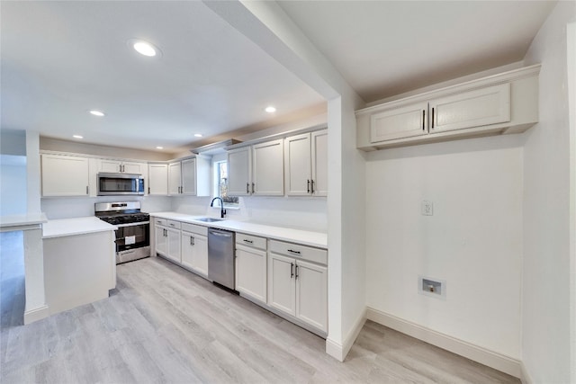 kitchen with appliances with stainless steel finishes, light hardwood / wood-style floors, sink, and white cabinetry