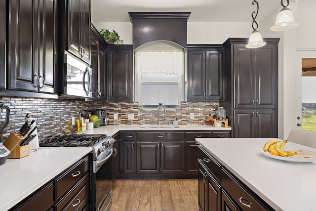 kitchen featuring appliances with stainless steel finishes, tasteful backsplash, sink, light wood-type flooring, and hanging light fixtures