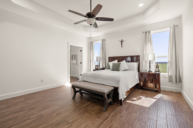 bedroom with ceiling fan, a raised ceiling, and dark wood-type flooring