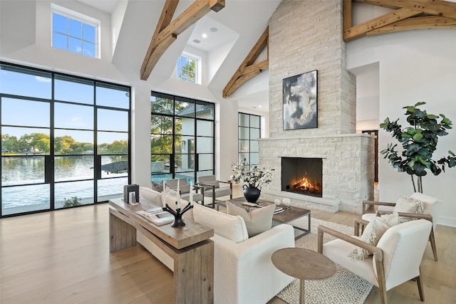 living room with high vaulted ceiling, a water view, light wood-type flooring, a fireplace, and beamed ceiling