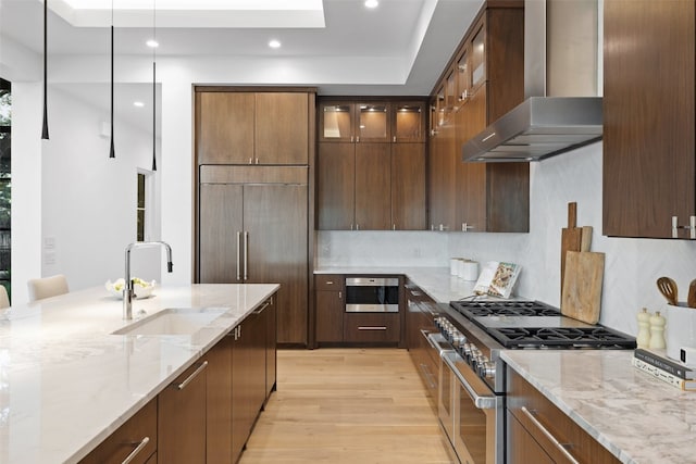 kitchen featuring light stone counters, wall chimney exhaust hood, stainless steel appliances, sink, and light hardwood / wood-style floors