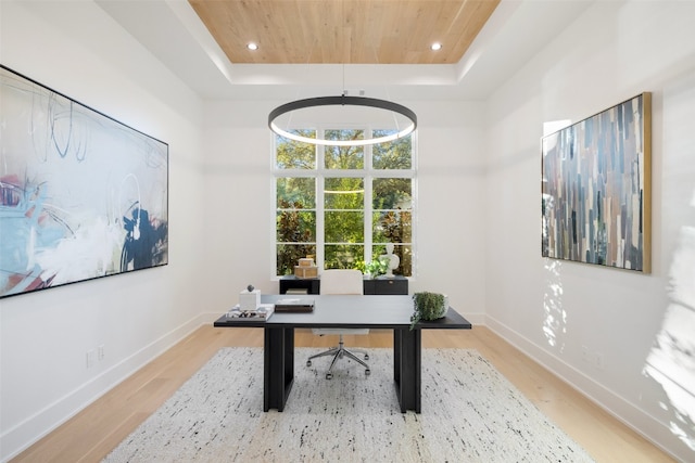 office space featuring a tray ceiling, light hardwood / wood-style flooring, wooden ceiling, and a high ceiling