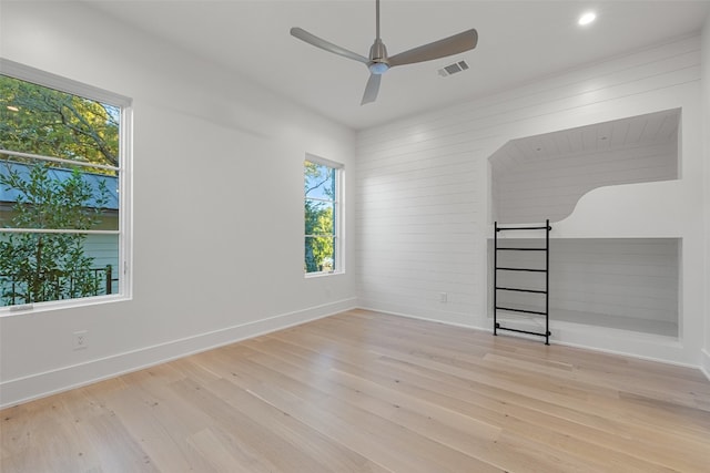 empty room with ceiling fan, a wealth of natural light, and light hardwood / wood-style flooring