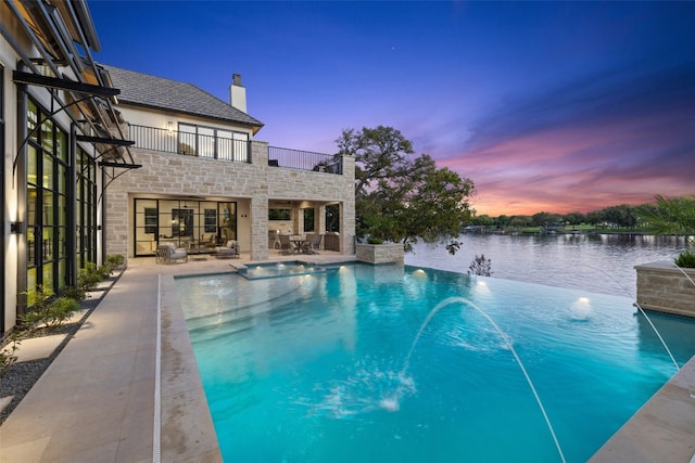 pool at dusk with an in ground hot tub, outdoor lounge area, pool water feature, a water view, and a patio